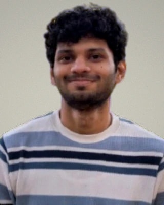 Nikhil Savant im blau-weiß gestreiften Pullover vor hellgrauem Grund